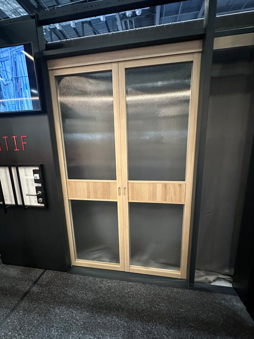 A pair of modern double doors with light wood frames and frosted glass panels, set within a dark display structure.
