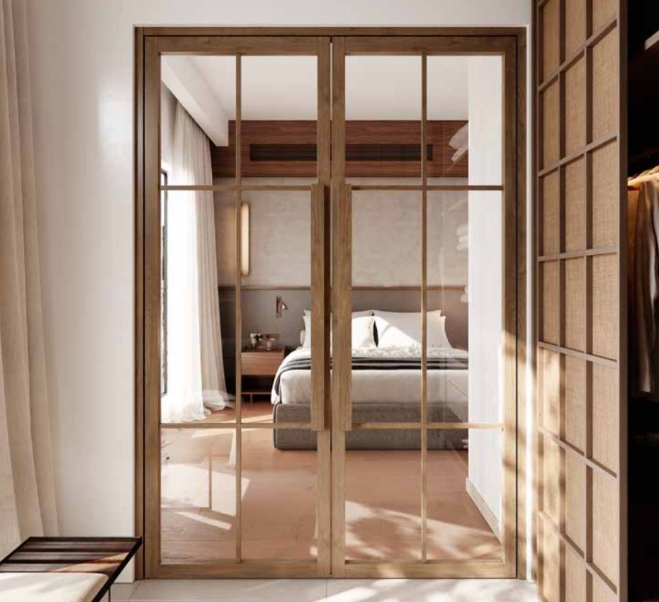 Wood-framed glass sliding doors with a grid pattern, separating a bright bedroom from a sunlit interior space. The bedroom features a neatly made bed with white linens, a wooden nightstand, and warm neutral walls.